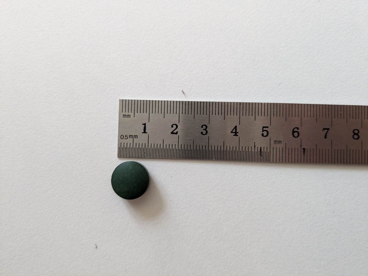 Närbild av spirulinatablett bredvid linjal cirka 11 mm, egen testbild