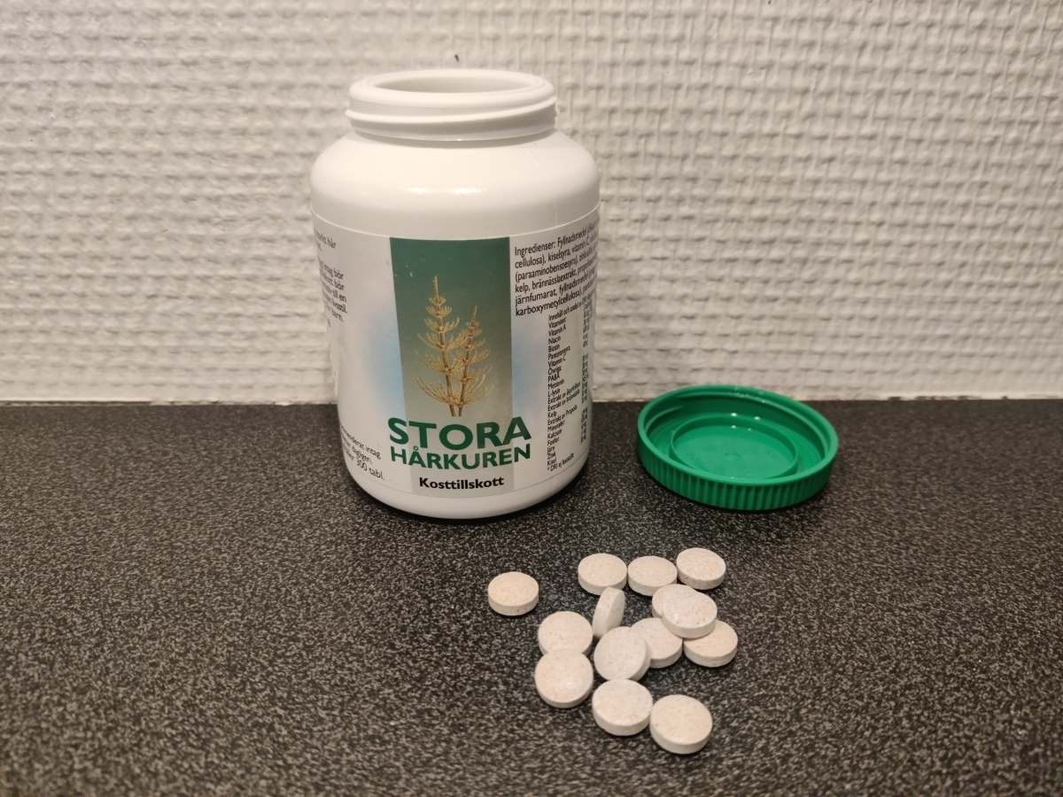 Öppnad burk Stora Hårkuren med små ljusa tabletter och grönt lock bredvid, foto taget av oss under testet